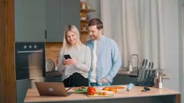 Sağlıklı Asyalı genç çift evlerinde hafif bir iç mekanda yemek pişiriyor ve cep telefonu kullanıyor.