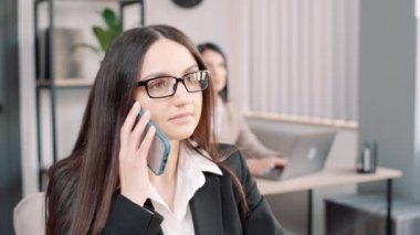 Yakın çekim. Genç, meşgul bir iş kadını. Proje evrakları üzerinde çalışıyor. Telefonda konuşuyor. Ofiste çalışan bir takımda çalışan yapışkan notlar üzerine mobil yazma görevleri üzerine iş görüşmesi yapan kadın yönetici