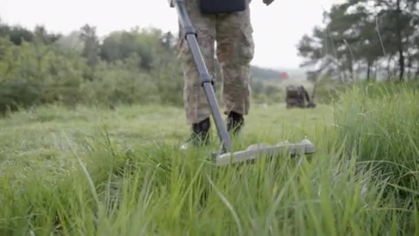 現場に金属探知機付きの軍用スパップ ウクライナ爆発兵器処理官金属探知機で金属を検出 防護ヘルメットと装備を着た男が — ストック動画