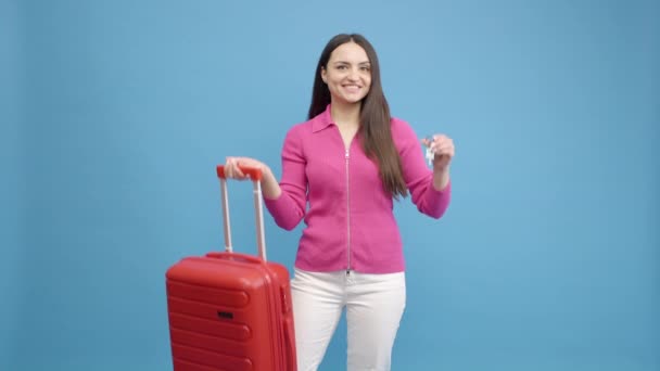 青い背景には フライトスーツケースとキーを手にした女の子の旅行者 スローモーション — ストック動画