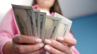Kapalı çekimde kadın eller 100 dolarlık banknotları sayıyor. Bir iş kadını nakit sayıyor. Yatırım, para değişimi, rüşvet ya da yolsuzluk kavramı. Mavi arkaplan