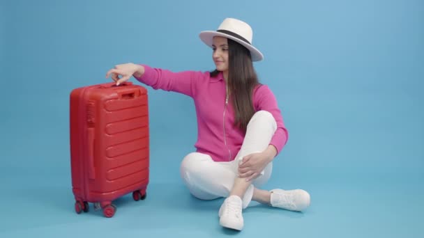 白い帽子の陽気な白人の女の子は 旅の出発の準備をして スーツケースと休暇旅行に出発します 幸せな女性座ってスピン赤ブリーフケース荷物 — ストック動画