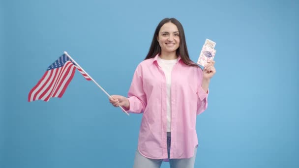 幸せな愛国心の少女は アメリカの国旗を振って笑顔 パスポートとドルを保持し 独立記念日の国民の休日 民主主義を祝う 青い背景に隔離された屋内スタジオショット — ストック動画