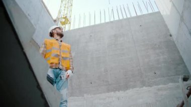 İnşaat alanında alet çantası ve balon seviyesinde aleti olan erkek işçi yan tarafa bakıyor. Yavaş çekim