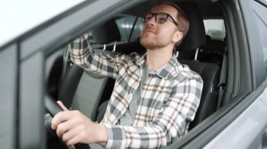 Portrait of a happy young man driving a new luxury electric car in a car dealership. The man shows emotions of happiness while driving in her new car. The buyer selects a car