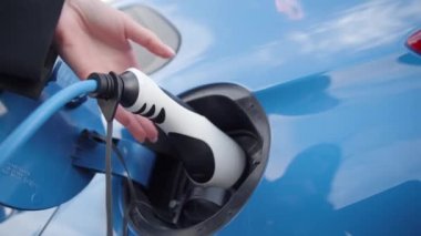 Kafkasyalı kadının elektrikli arabanın şarj prizinden şarj aletini çıkartırken yakın çekimi. Yavaş çekim