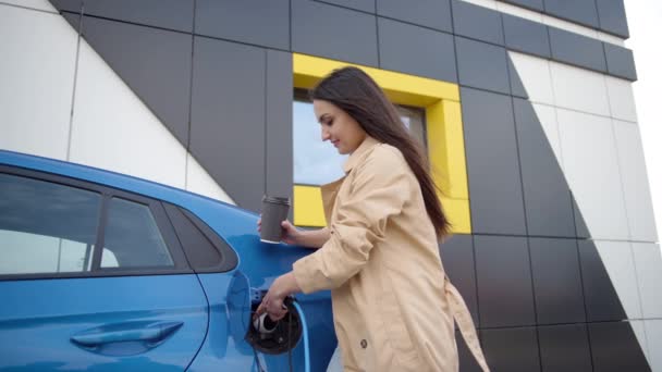 Kadın Şarj Aletini Şarj Prizine Takıyor Elektrikli Arabasının Yanında Kahveyle — Stok video