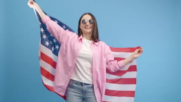 アメリカの眼鏡を振って アメリカの国旗に包まれた幸せな笑顔の女の子は 人権と自由を祝う 独立記念日 — ストック動画