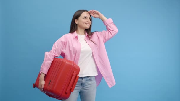 Χαμογελαστή Γυναίκα Κάνει Διαφήμιση Στο Στούντιο Μπλε Φόντο Κόκκινη Βαλίτσα — Αρχείο Βίντεο