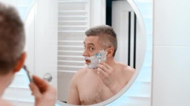 Ustura tıraşlı erkek suratı. Beyaz bir adam traş makinesiyle yüzünü tıraş ediyor. Sakalı kes. Sakal tıraşı. Tıraşsız adam sakalını kesti.