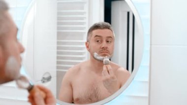 Aynaya bak, tıraş köpüğü, hijyen, güzellik ve cilt bakımını sabah rutiniyle yap. Evdeki tuvalette köpüklü mutlu bir erkek.