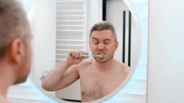Genç adam banyoda dişlerini fırçalıyor. Sabah erkeğinin prosedürleri aynada.