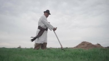 Ukrayna nakışlı gömlekli yaşlı bir adam tarladaki çimleri biçiyor. Yavaş çekim