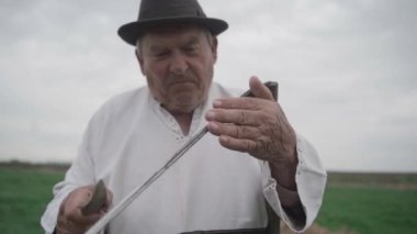 Yaşlı adam tarlada eski bir tırpanı keskinleştirir. Yavaş çekim
