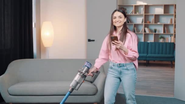 Młoda Dziewczyna Trzyma Telefon Komórkowy Patrzy Kamerę Podczas Sprzątania Salonu — Wideo stockowe