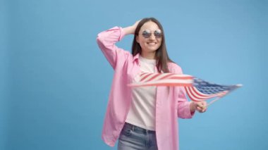 Amerika bayrağı ve mavi arka planda izole edilmiş Amerikan gözlükleriyle gülümseyen beyaz kadın. Kadın duygularını ve dansını gösterir.