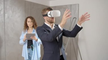 Takım elbiseli genç adam ve kadın tasarımcılar yenileme sırasında yeni bir dairede duruyorlar. VR gözlükleri takıyorlar. Ev, sanal gerçeklik, yenileme konsepti tasarlamak için fütüristik teknolojiler kullanıyorlar.