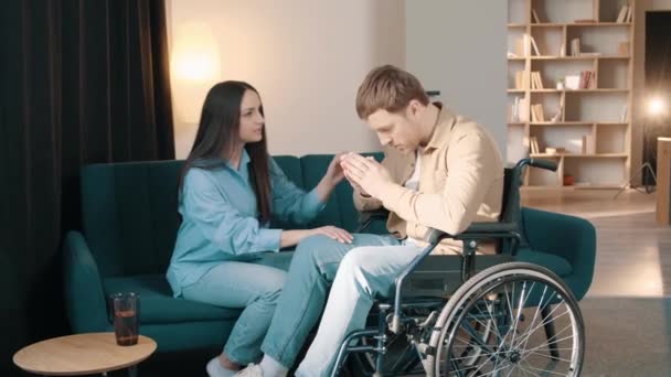 Заботливая Молодая Жена Положить Руку Мужа Сидящего Инвалидной Коляске Дому — стоковое видео