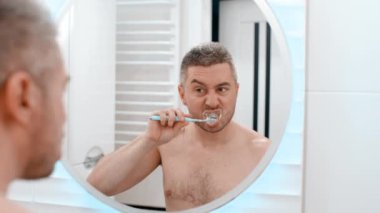 Genç adam banyoda dişlerini fırçalıyor.