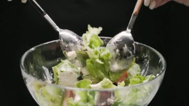 Metalik kaşıklar salatayı cam tabakta salatayla karıştırır. Salatalıklar, feta vejetaryen yemekleri.
