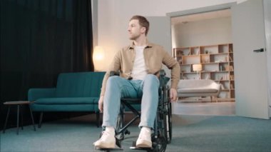 Odasında tekerlekli sandalyede oturan beyaz bir adam pencereden dışarı bakıyor.