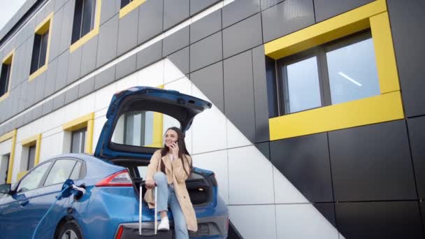 Blanke Vrouw Zittend Kofferbak Van Haar Elektrische Auto Met Mobiele — Stockvideo
