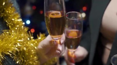 Parlak çelenkle süslenmiş Noel ağacına karşı şampanya kadehleriyle tezahürat eden insanların elleri. Bulanık arkaplan, bokeh
