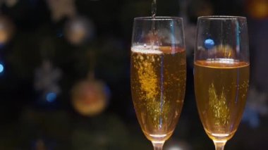 Kutlama dekorasyonlarının, ışıkların ve yılbaşı ağacının arka planına karşı köpüren iki şampanya bardağının kapanışı