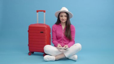 Seyahat bütçesi konsepti. Kırmızı valizli mutlu kadın para ve seyahat evraklarını gösteriyor ve çıkış turuna çıkmaya hazır.