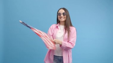 Amerikan gözlüklü, modaya uygun genç kız Amerikan bayrağı sallıyor, kutluyor, insan hakları ve özgürlüklerini kutluyor. Bağımsızlık Günü. Dişi dans ediyor.
