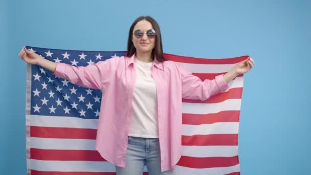 アメリカの眼鏡を振って アメリカの国旗に包まれた幸せな笑顔の女の子は 人権と自由を祝う 独立記念日 — ストック動画