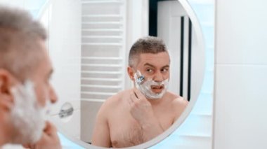 Ustura tıraşlı erkek suratı. Beyaz bir adam traş makinesiyle yüzünü tıraş ediyor. Sakalı kes. Tıraşsız adam sakalını kesti.