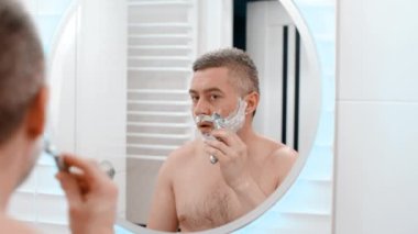 Ustura tıraşlı erkek suratı. Beyaz bir adam traş makinesiyle yüzünü tıraş ediyor. Sakalı kes. Tıraşsız adam sakalını kesti.