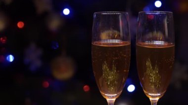 Kutlama dekorasyonlarının, ışıkların ve yılbaşı ağacının arka planına karşı köpüren iki şampanya bardağının kapanışı