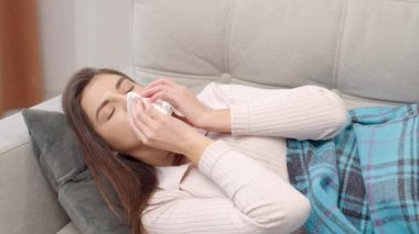 Mendilin içine hapşıran genç bir kadın, akan burnunu siliyor. Hasta kız grip olmuş ya da nezle olmuş. Alerji belirtileri gösteriyor.