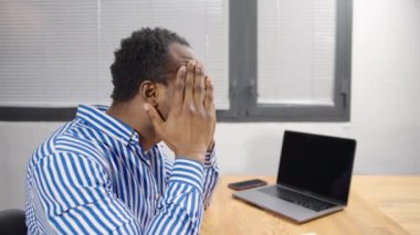 Ofiste çalışan, bilgisayarlı, stresli ve üzgün Afro-Amerikan bir adam.