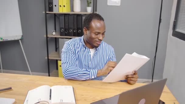 有文件 收到信件 阅读法律文件 审查项目报告 坐在办公室笔记本电脑旁的专注的非洲年轻雇员 — 图库视频影像
