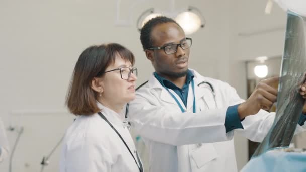 Beyaz Önlüklü Siyah Adam Kadın Tıbbi Ameliyathanede Röntgen Görüntülerini Inceliyor — Stok video