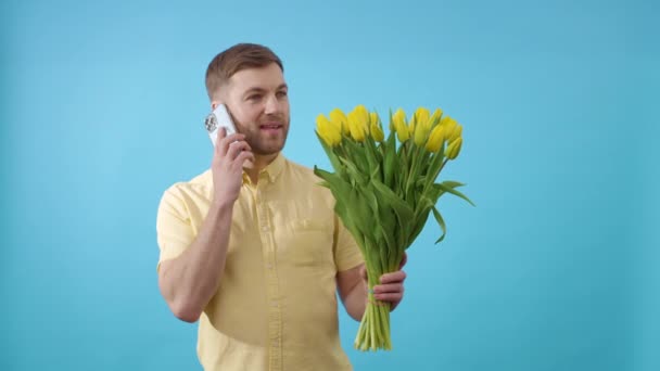 Mężczyzna Mówi Przez Telefon Komórkowy Trzymając Bukiet Żółtych Tulipanów Niebieskim — Wideo stockowe