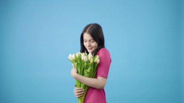 Mavi arka planda beyaz laleler tutan bir kadın.