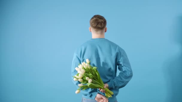 笑脸的男人转过脸来 拿出一束蓝色背景的白郁金香 — 图库视频影像