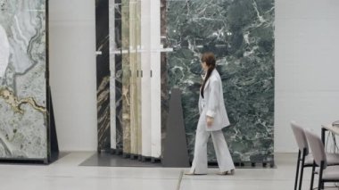 Sergi salonundaki mermer duvarın önünde yürüyen kadın.