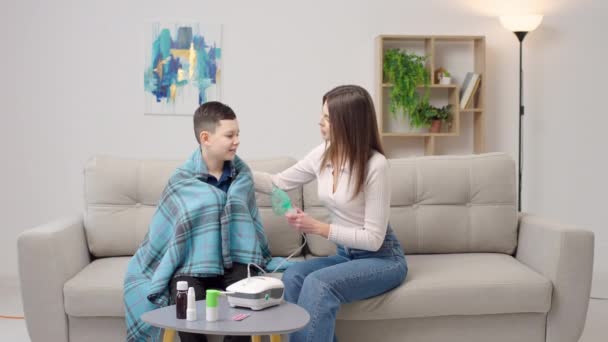 母亲帮助生病的儿子在家里抱着他睡沙发时使用了雾化剂 女人用设备吸入男孩 — 图库视频影像