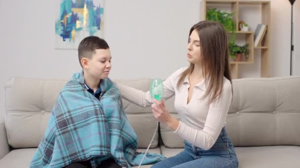 母亲帮助生病的儿子在家里抱着他睡沙发时使用了雾化剂 女人用设备吸入男孩 — 图库视频影像