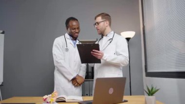 Beyaz önlüklü iki doktor hastane ofisinde test sonuçlarını tartışıyor.