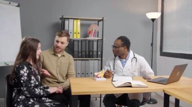 Baba ve kızı hastane ofisinde siyahi bir doktorla görüşüyorlar.