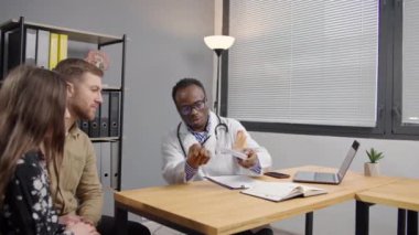 Baba ve kızı hastane ofisinde siyahi bir doktorla görüşüyorlar.
