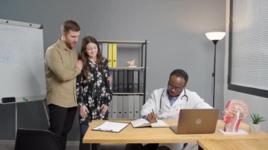 Genç bir adam ve kızı, doktor ofisinde siyahi bir doktorla konuşuyorlar.