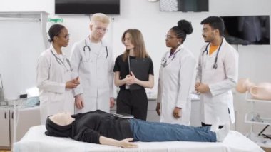 Bir grup doktor ilk yardım dersinde profesyonel bir hemşireyi dinliyor ve klinikteki kameraya bakıyor.