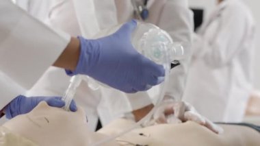 Beyaz önlüklü ve mavi eldivenli biri klinikteki mankenlere ilk yardım yapıyor.